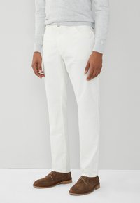 Pantalones de algodón blancos con corte recto, que cuentan con dos bolsillos y cierres metálicos, combinados con zapatos de ante marrones.