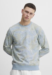 Lyseblå sweatshirt med et bladmønster i gr�øn og hvid. Den har rund hals, lange ærmer og en kontrastfarvet ribbet kant.