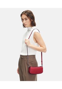 Czerwona skórzana torba na ramię o eleganckim designie i regulowanym pasku. Charakteryzuje się gładką teksturą i subtelnym logo z przodu.