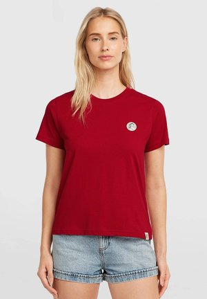 Rood katoenen T-shirt met een ronde hals en korte mouwen, met een klein circulair logo op de linkerborst. Gecombineerd met lichte denim shorts.