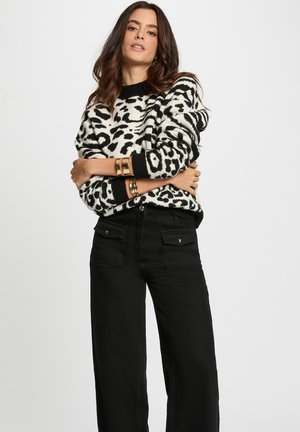 Un pull en motif léopard noir et blanc avec un col côtelé, porté sur un pantalon large taille haute noir avec des poches avant.