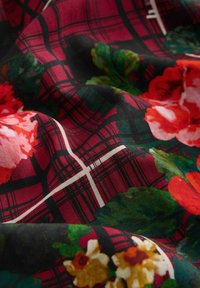 Cotton fabric featuring a red and black plaid pattern with large, vibrant flowers in shades of red, pink, and green. Soft texture.