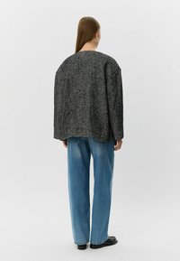 Černobílé oversized sako s herringbone vzorem a kulatým výstřihem, v kombinaci s volnými modrými džínami a černými botami.