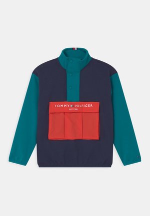 Giacca a maglione in navy, teal e rosso, con colletto alto, bottoni a pressione, tasca frontale e logo "TOMMY HILFIGER EST. 1985".