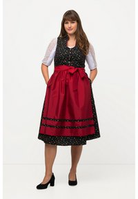 Vêtement traditionnel avec un corsage noir à motifs floraux et un tablier en satin rouge. Présente une taille ceinturée et une jupe à mi-mollet, assortie à des talons noirs.