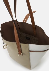 Sac cabas en cuir bicolore beige et blanc avec des anses en cuir marron, ouverture supérieure laissant voir une poche intérieure zippée et l'étiquette de la marque Furla.