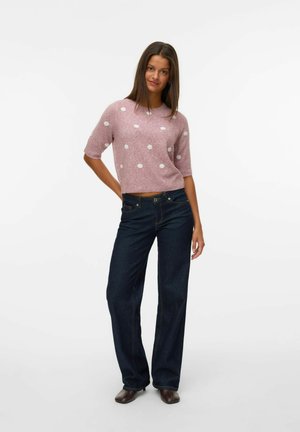 Pull léger rose avec des pois blancs, à manches courtes et coupe décontractée, associé à un jean ample bleu foncé. Bottines marron.