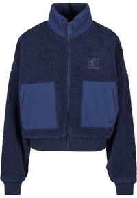 Marinblå kort jacka gjord av mjuk, texturerad fleece med hög krage, dragkedjestängning och två fickor av applikation i en kontrasterande tyg.