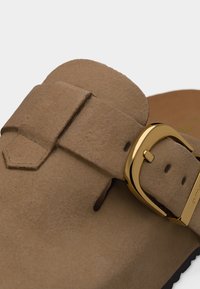 Sandale en daim marron avec une large bride, une boucle en or et des trous réglables.