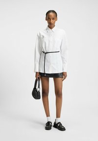White button-up shirt with a black belt, paired with a black leather mini skirt. Black shoulder bag and shoes with textured detailing.