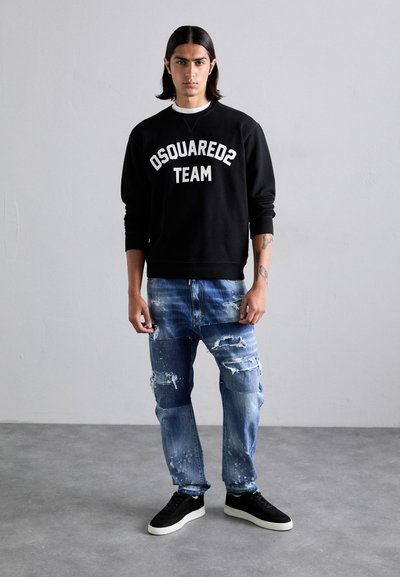 Hanorac negru cu text alb "DSQUARED2 TEAM", asortat cu blugi albaştri distruşi, cu petice şi un croi relaxat. Tenisi negri completează ţinuta.