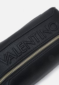 Borsa nera in pelle con logo in rilievo "VALENTINO" e una cerniera dorata. Superficie testurizzata con una forma strutturata e bordi arrotondati.