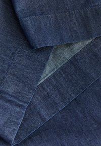 Κοντινό πλάνο διπλωμένου σκουρόμπλε τζιν υφάσματος που δείχνει τις ραφές και τις λεπτομέρειες της υφής.