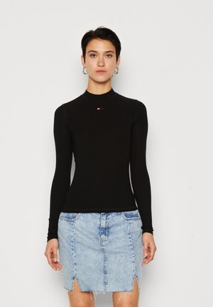 Black long-sleeve top with a high neck, featuring a small logo. Paired with a light blue denim skirt with side slits and a frayed hem.