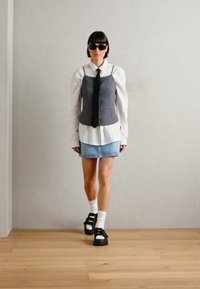 Gilet grigio, camicia bianca con bottoni, minigonna in denim, cravatta nera e scarpe con zeppa nere. Gli accessori includono occhiali da sole scuri e calzini bianchi.