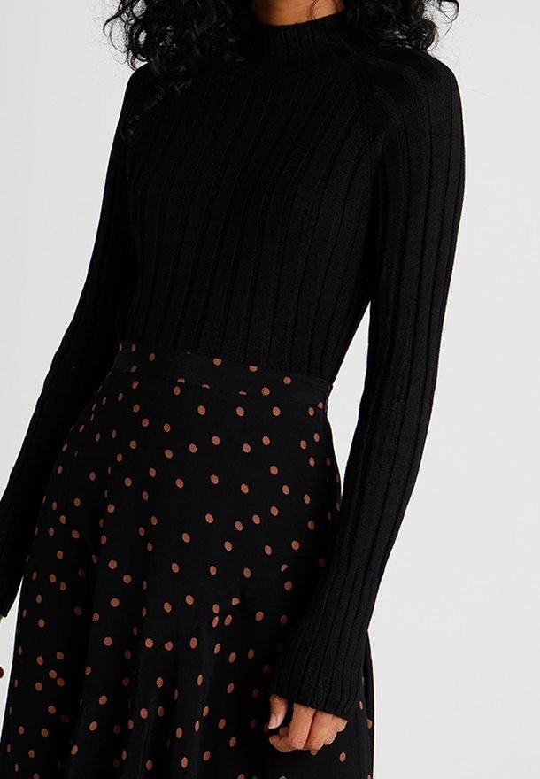Schwarzer gerippter Rollkragenpullover mit langen Ärmeln, kombiniert mit einem schwarzen Rock mit braunen Punkten, der ein kontrastierendes Muster erzeugt.