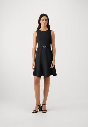 Black sleeveless dress with a fitted bodice, flared skirt, and a decorative belt. Worn with black heeled sandals. Smooth texture.