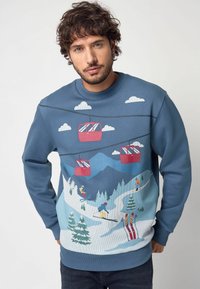 Modrá mikina s designem lyžařského střediska, obsahující grafiku lanovek, hor, stromů a lyžařů; vyrobená z měkké, texturované tkaniny.