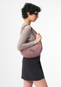 Hobo-Tasche aus weichem mauvefarbenem Stoff, mit runder Form, zwei schwarzen runden Akzenten und einem langen Schultergurt.