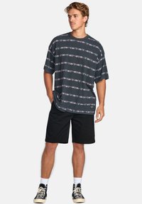 Dark gray t-shirt with horizontal floral patterns in pink. Loose fit, round neckline. Paired with black shorts and high-top sneakers.