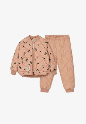 Veste matelassée de couleur pêche avec des motifs floraux sombres, associée à un pantalon assorti. Dispose de poignets côtelés et d'une fermeture éclair à l'avant.