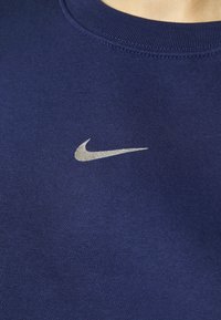 Mörkblå sweatshirt med en silver Nike Swoosh-logotyp, tillverkad av mjukt tyg med rundad halsringning och ribbade ärmslut.