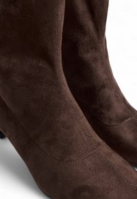 Botas de ante marrón hasta la rodilla con una textura suave, diseño ajustado y sutiles detalles de costura a lo largo de los lados. Tacones bajos en bloque.
