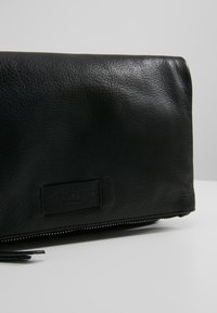 Černá kožená kabelka s texturovaným povrchem, se zipovým uzávěrem a logem. Jednoduchý obdélníkový tvar s čistým designem.