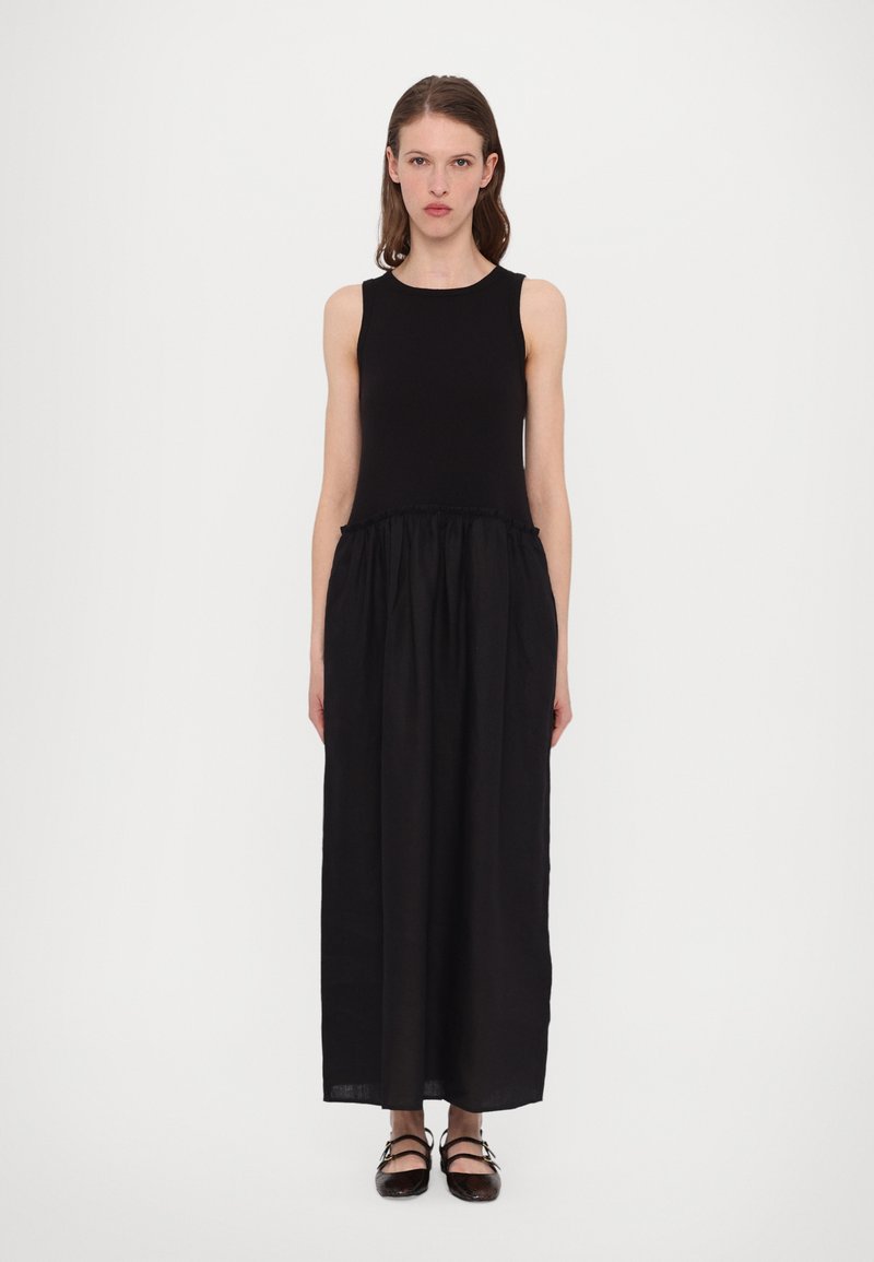Robe maxi noire avec un haut sans manches, un corsage ajusté et une jupe froncée. Fabriquée dans un tissu léger au toucher doux. Chaussures plates à lanières.