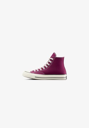 Zapatilla de lona morada de caña alta con cordones blancos y suela de goma, vista de lado sobre un fondo blanco.