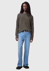 Dark green textured knit sweater, light blue jeans, black belt, black slip-on shoes. Straight-leg jeans with fading. Long dreadlocks.
