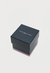 Dark navy square box with a lid, featuring "TOMMY HILFIGER" text in white. Red, white, and blue accents on the base. Smooth texture.