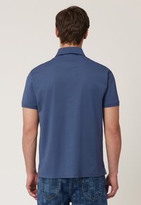 Marinblå polo skjorta med klassisk krage, korta ärmar och rak nederkant, tillverkad av mjukt bomullstyg. Bärs med mönstrade blå jeans.