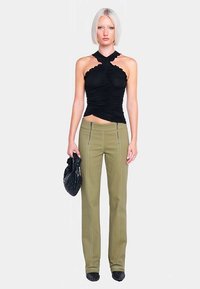 Haut noir froncé à col licou associé à un pantalon vert olive, avec des coutures contrastantes et une coupe ajustée, complété par un sac noir.