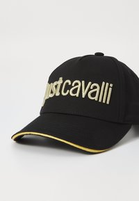 Black baseball cap with embroidered "justcavalli" logo in gold, featuring a curved visor with a gold accent along the edge.