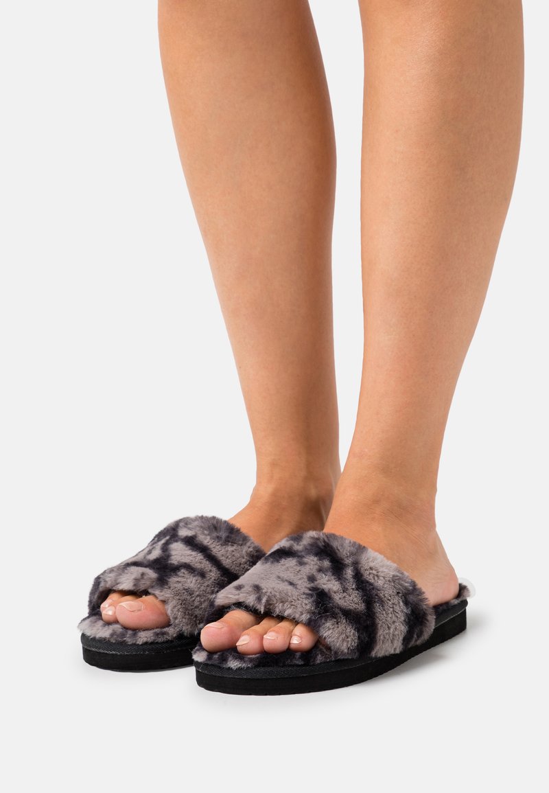 Faux fur slide sandals in grey with black pattern, featuring a wide strap and a cushioned black sole. Suitable for indoor wear.