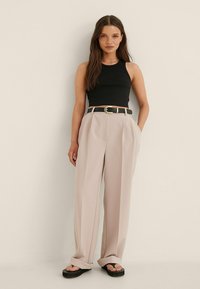 Black fitted sleeveless top paired with loose beige trousers, cinched with a black belt featuring a gold buckle. Worn with flat black sandals.