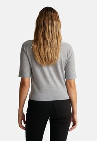 Szary sweter z krótkim rękawem o dopasowanym kroju i strukturalnej teksturze, noszony z czarnymi dżinsami. Gładki materiał bez widocznych wzorów czy elementów metalowych.