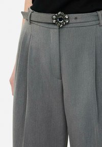 Gray tailored trousers with a smooth texture, featuring a decorative belt buckle with crystal accents and a central dark gemstone.