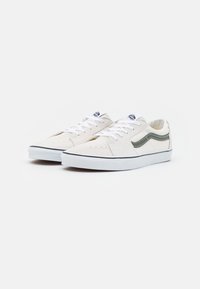 Białe zamszowe sneakersy z zielonym paskiem, białymi sznurowadłami i gumową podeszwą. Posiadają perforowane detale na palcach oraz logo na języku.
