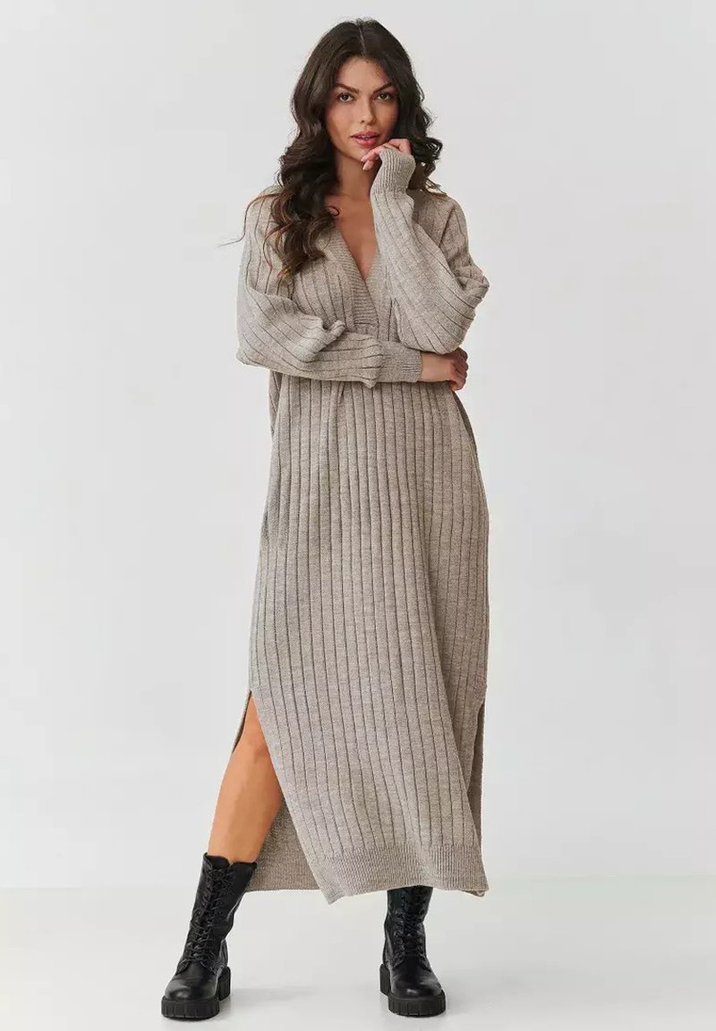 Długa, prążkowana dzianinowa sukienka w jasnoszarym kolorze z głębokim dekoltem w kształcie litery V i bocznymi rozcięciami. W zestawie z czarnymi, masywnymi butami na sznurowania. Miękka tekstura.