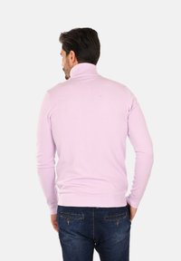 Maglione a collo alto di colore viola chiaro, realizzato in materiale morbido, con design aderente, colletto e polsini a costine. Abbinato a pantaloni in denim scuro.