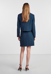 Modrý kostkovaný blazer a sukně, strukturovaná látka, přiléhavý design, zkrácená bunda a elegantní sandály na podpatku s páskem kolem kotníku.