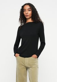 Zwarte langemouwtop met een ronde halslijn, gemaakt van een glad materiaal, gecombineerd met lichtgekleurde ribcordbroeken.