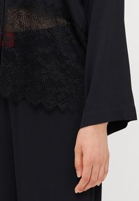 Black garment featuring lace accents, a smooth texture, and wide sleeves, showcasing intricate patterns and a subtle, elegant design.