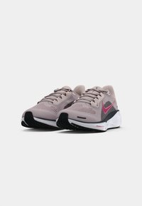 Une paire de chaussures de course Nike rose et noire avec des semelles blanches sur un fond clair uni, inclinées pour montrer l'avant et les côtés.