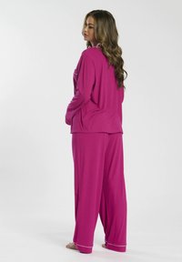 Conjunto de loungewear rosa, que incluye una blusa de manga larga con un bolsillo y pantalones de corte holgado. Tejido suave y liso con costuras de acento en blanco.