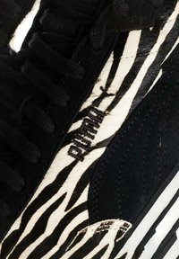 Sneaker bianco e nero con stampa zebra su materiale in pelliccia, dettagli in suede nero, lacci piatti e logo marchiato in cucitura nera.