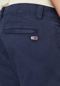 Mörkblå chinos med en mjuk textur, utrustade med en bakficka och en liten broderad logotyp i rött, vitt och blått.