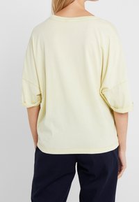 Camiseta de manga corta amarillo claro con un corte holgado, cuello redondo y puños enrollados, hecha de una suave mezcla de algodón.